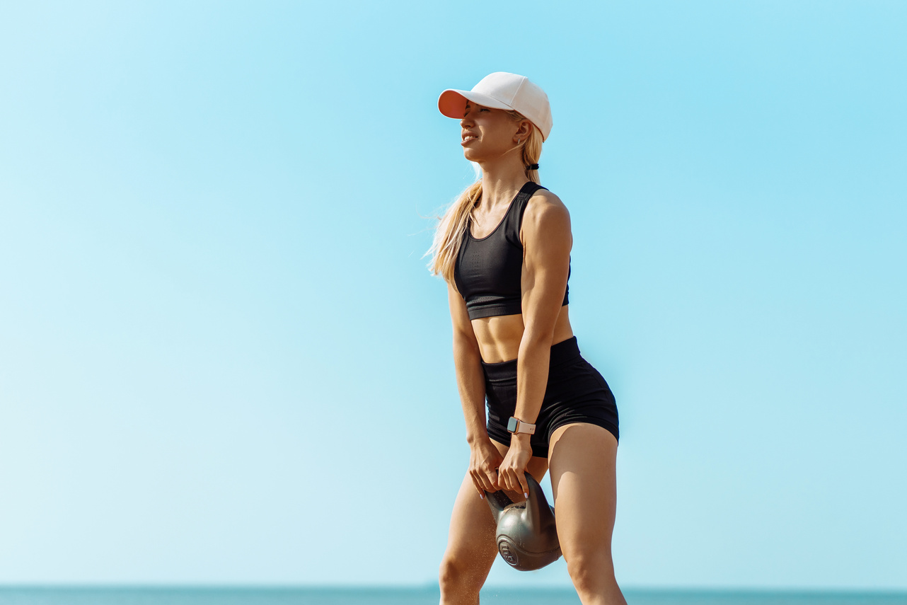 Sportswoman in Sportswear Lifting Weights, Sportive Woman Holding a Kettlebell during Crossfit Workout, on the Beach